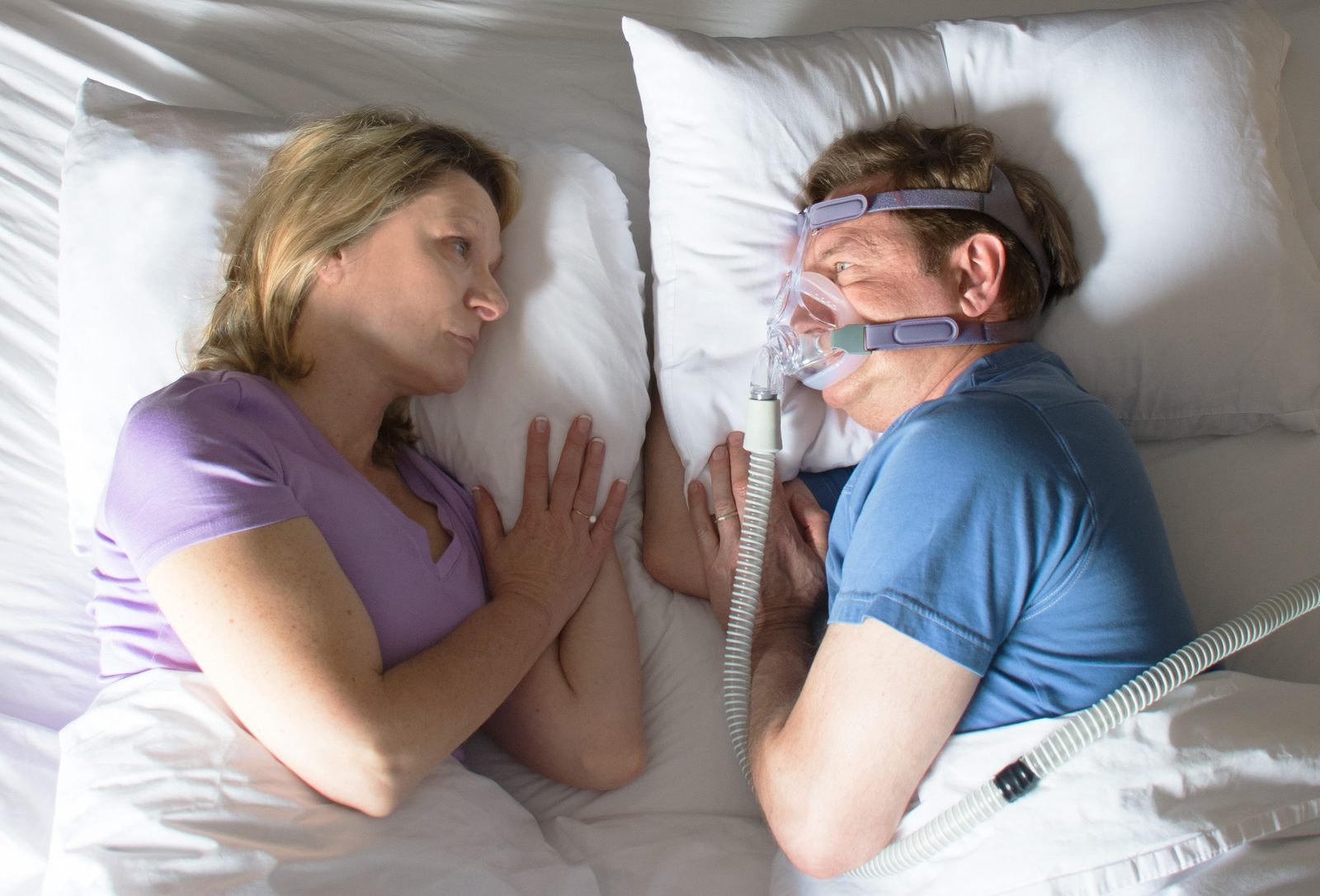 A couple in bed, one of them wearing a CPAP mask
